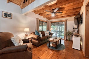 A cozy living room with wooden floors and a ceiling fan, furnished with a sofa, armchair, and coffee table.