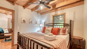 A cozy bedroom with a wooden bed, a ceiling fan, and a window with a view of greenery. - River Ben -  2-bedroom cabin in serene Suches with AC (Suches)