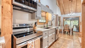 A modern kitchen with a large stove, wooden cabinets, and a dining area with a table and chairs. - River Ben -  2-bedroom cabin in serene Suches with AC (Suches)