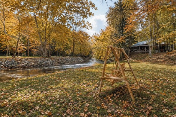 Une balançoire en bois, installée dans un cadre naturel, avec une rivière et des arbres aux couleurs automnales.