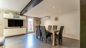 A modern dining area with a wooden table and chairs, a built-in TV, and a large window. - Villa 'Chez Marco' with Private Terrace, Wi-Fi, and Air Conditioning (Saint-Rémy-de-Provence)