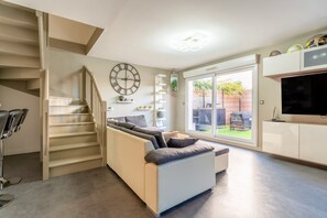 A living room with a sofa, a staircase, a TV, and a large window. - Villa 'Chez Marco' with Private Terrace, Wi-Fi and Air Conditioning (Saint-Rémy-de-Provence)