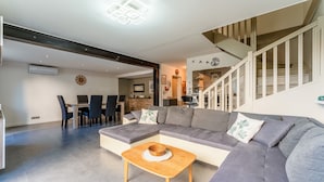 A modern living room with a sectional sofa, a dining table with chairs, a staircase, and a ceiling light fixture. - Villa 'Chez Marco' with Private Terrace, Wi-Fi, and Air Conditioning (Saint-Rémy-de-Provence)