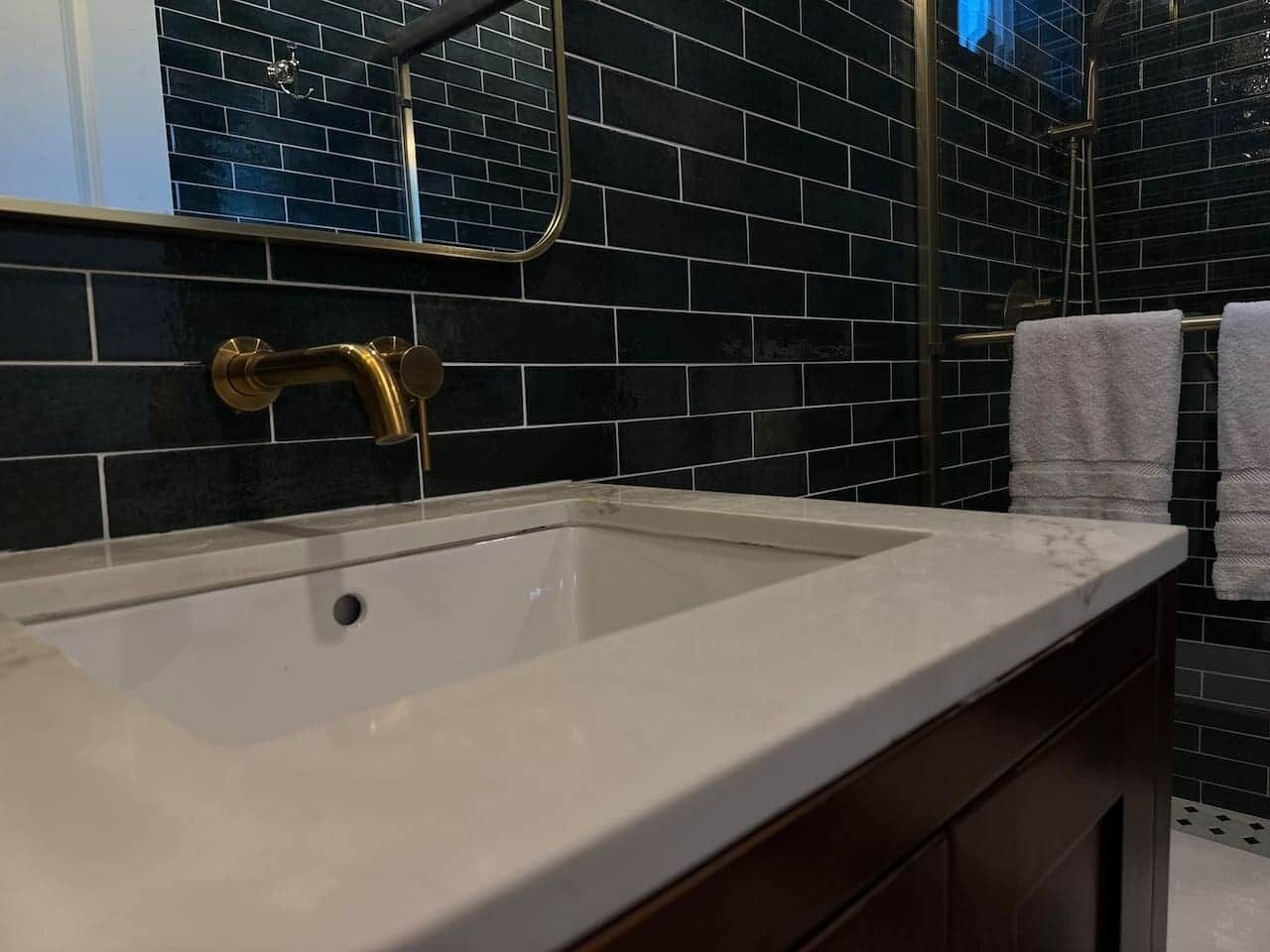 Une salle de bain avec un lavabo blanc, des murs recouverts de carreaux foncés et un porte-serviettes.