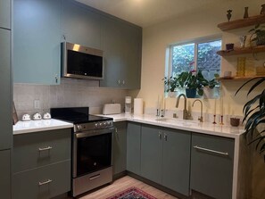A modern kitchen with grey cabinets, a stainless steel stove, a microwave, and a window with a view of greenery.