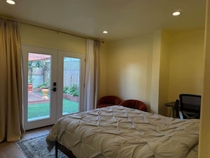 A bedroom with a bed, a chair, a desk, and a sliding glass door leading to a patio.