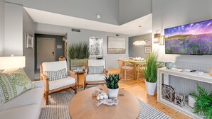Una sala de estar moderna con una mesa de centro redonda, sofás blancos, un televisor y varias plantas.