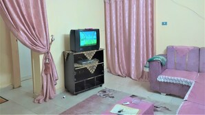 A living room with a television on a black stand, a pink sofa, and curtains. - Furnished apartment in Minya with archaeological tours (Minya Governorate)
