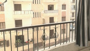 A balcony with a metal railing, overlooking a street with buildings that have multiple windows and balconies. - Furnished apartment in Minya with archaeological tours (Minya Governorate)
