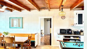 A dining area with a wooden table and chairs, a kitchen with a microwave and toaster, and a pool table. - 5 Min Walk to Beach! 4BR 2BA Classic Coastal Home - Sleeps 10, Space to Play! (North Myrtle Beach)