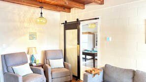 A cozy living room with two armchairs, a lamp, and a wooden coffee table. A sliding door leads to a dining area with a pool table. - 5 Min Walk to Beach! 4BR 2BA Classic Coastal Home - Sleeps 10, Space to Play! (North Myrtle Beach)
