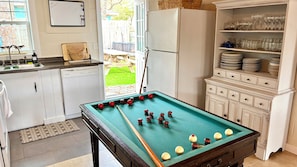 Une cuisine équipée d’une table de billard, d’un réfrigérateur et d’un meuble contenant de la vaisselle et des verres.