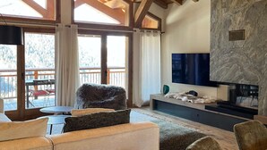 A spacious living area with a wooden ceiling, large windows, a stone accent wall, a flat-screen TV, and a cozy seating arrangement. - T4 spacieux avec cheminée (Peisey-Nancroix)