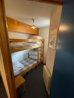 Une chambre avec un lit superposé, un petit banc en bois et un radiateur.