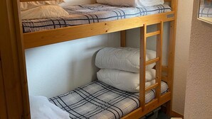 Una cama litera con estructura de madera, dos niveles de camas y una lámpara colgante.