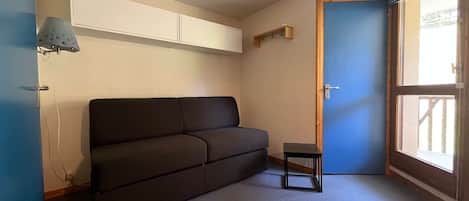 A small room with a dark-colored sofa, a small table, a door, and a window.
