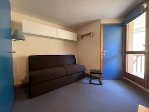 Une petite pièce avec un canapé de couleur sombre, une petite table, une porte et une fenêtre.