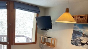 Una habitación acogedora con televisión, un aparador de madera, cama y ventana con vistas al exterior.