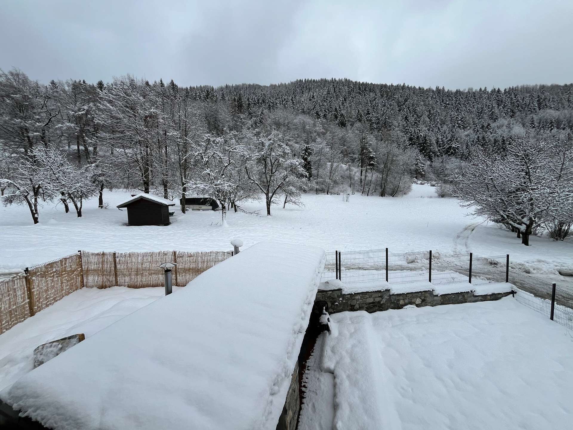 A snow-covered landscape with a wooden fence, a stone wall, and a small wooden structure.
