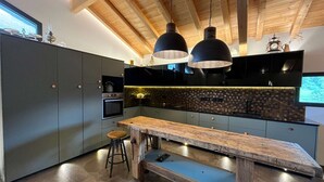 A modern kitchen with a wooden ceiling, black cabinets, a large island, and pendant lighting. - Chalet at the foot of the ski resorts with spa (Landry)