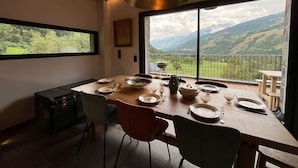 A dining area with a table set for four, a view of mountains through large windows, and a rustic wooden ceiling. - Chalet at the foot of the ski resorts with spa (Landry)