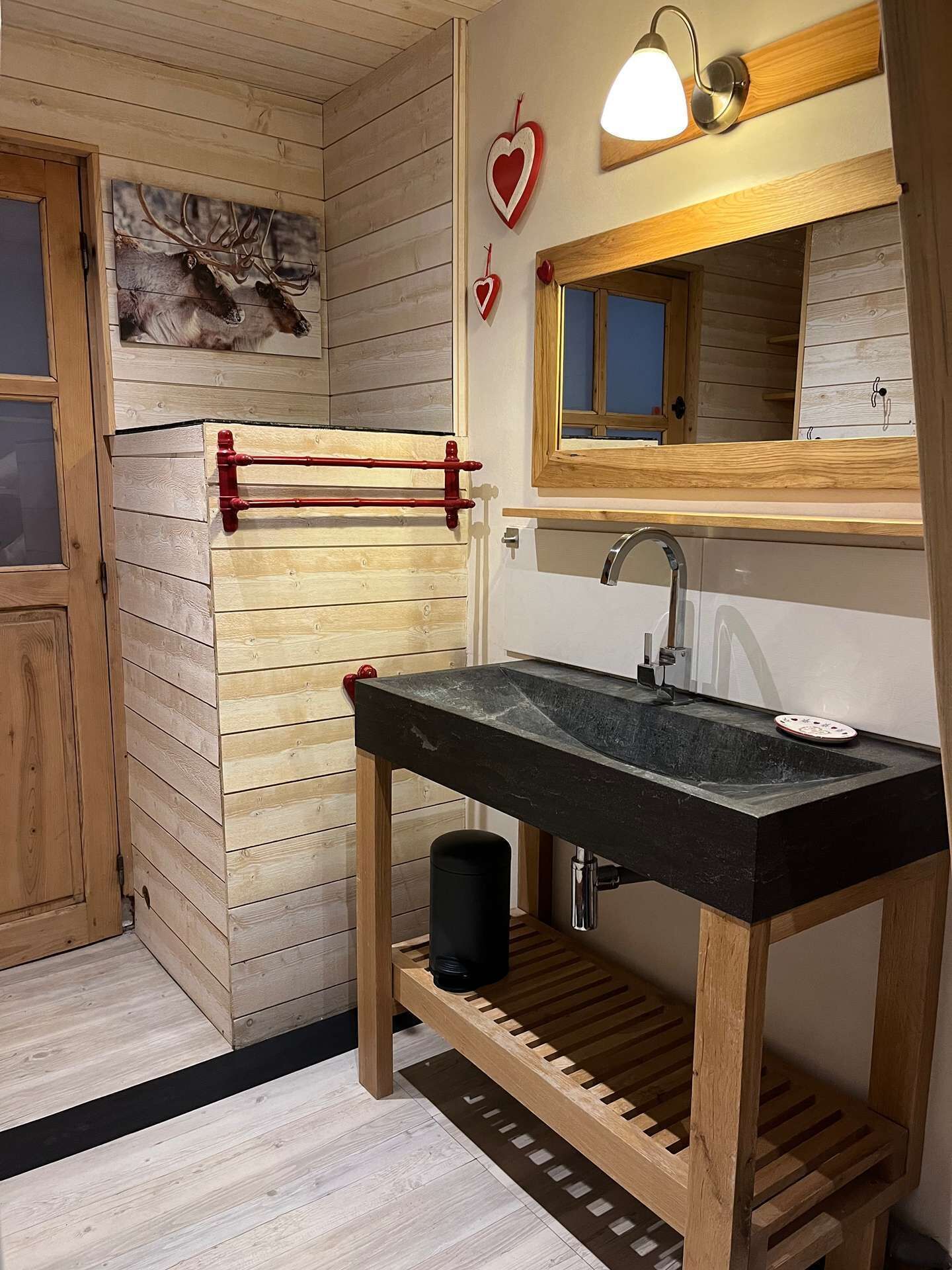 Un interior de madera con un lavabo negro, estanterías de madera, un perchero rojo y un espejo montado en la pared.