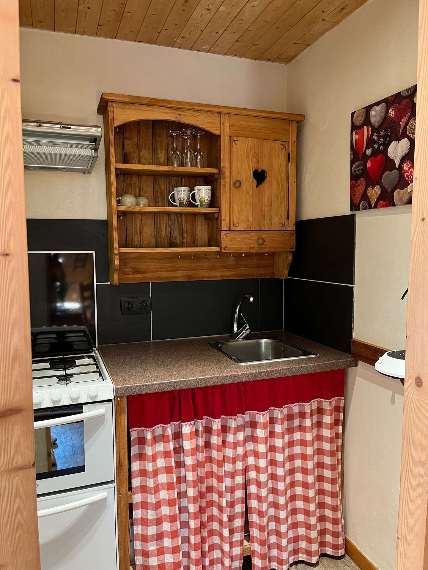 A compact kitchen with a gas stove, a sink, and a wooden cabinet above the countertop.