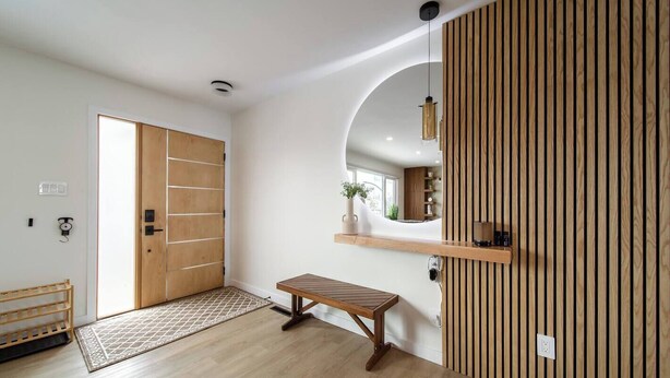 Un interior moderno con piso de madera, un banco, una puerta de madera y un espejo en la pared.
