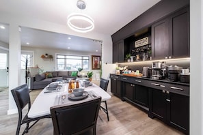 A modern kitchen with dark cabinetry, a dining area with a white table set for four, and a living room with a gray sofa and green cushions. - Relax, recharge, and play. Just 15 mins from Downtown Edmonton (Edmonton)
