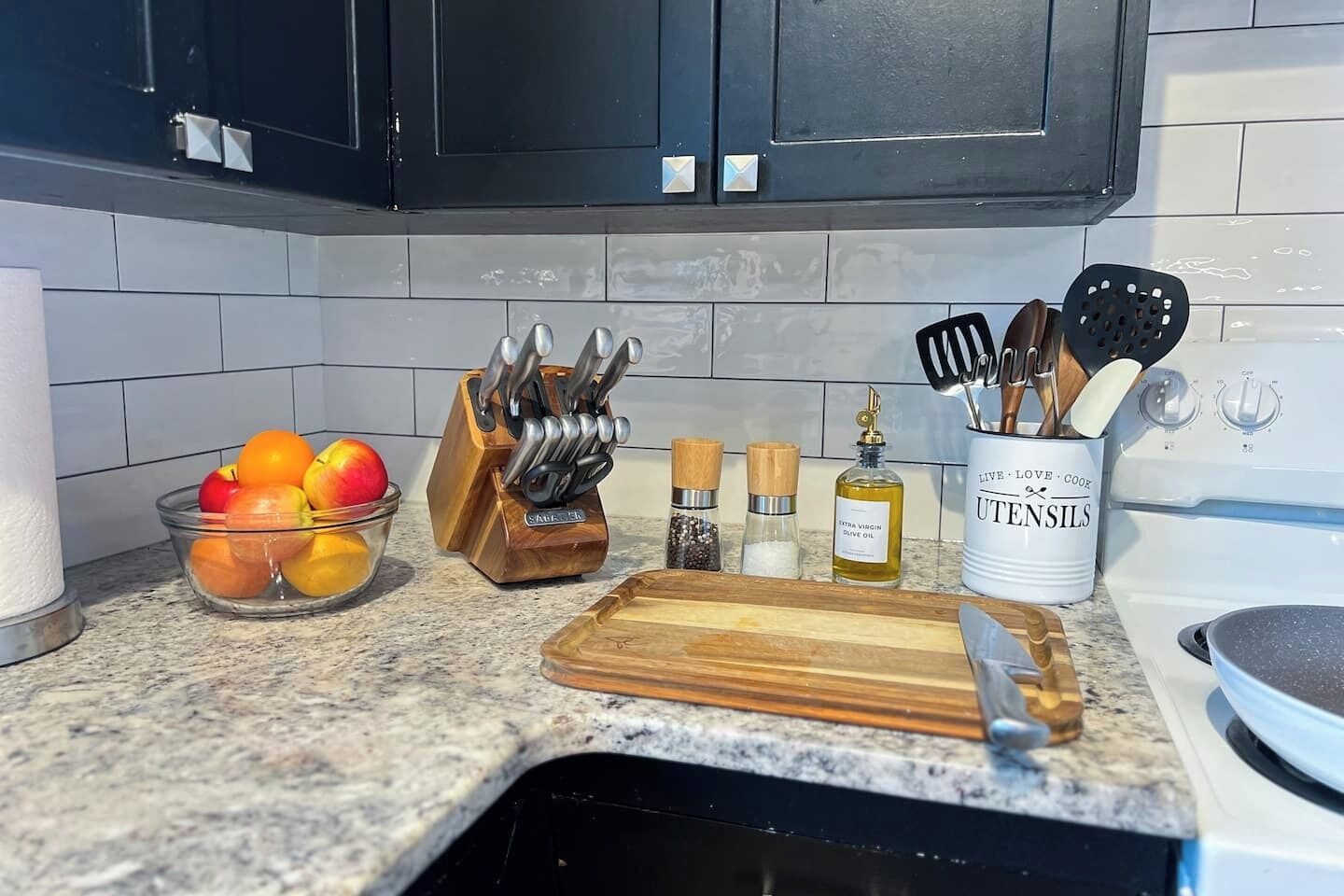 A kitchen counter with a fruit bowl, knife block, spice jars, and a utensil holder.