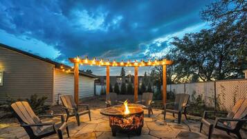 A patio with a fire pit, outdoor seating, and string lights.