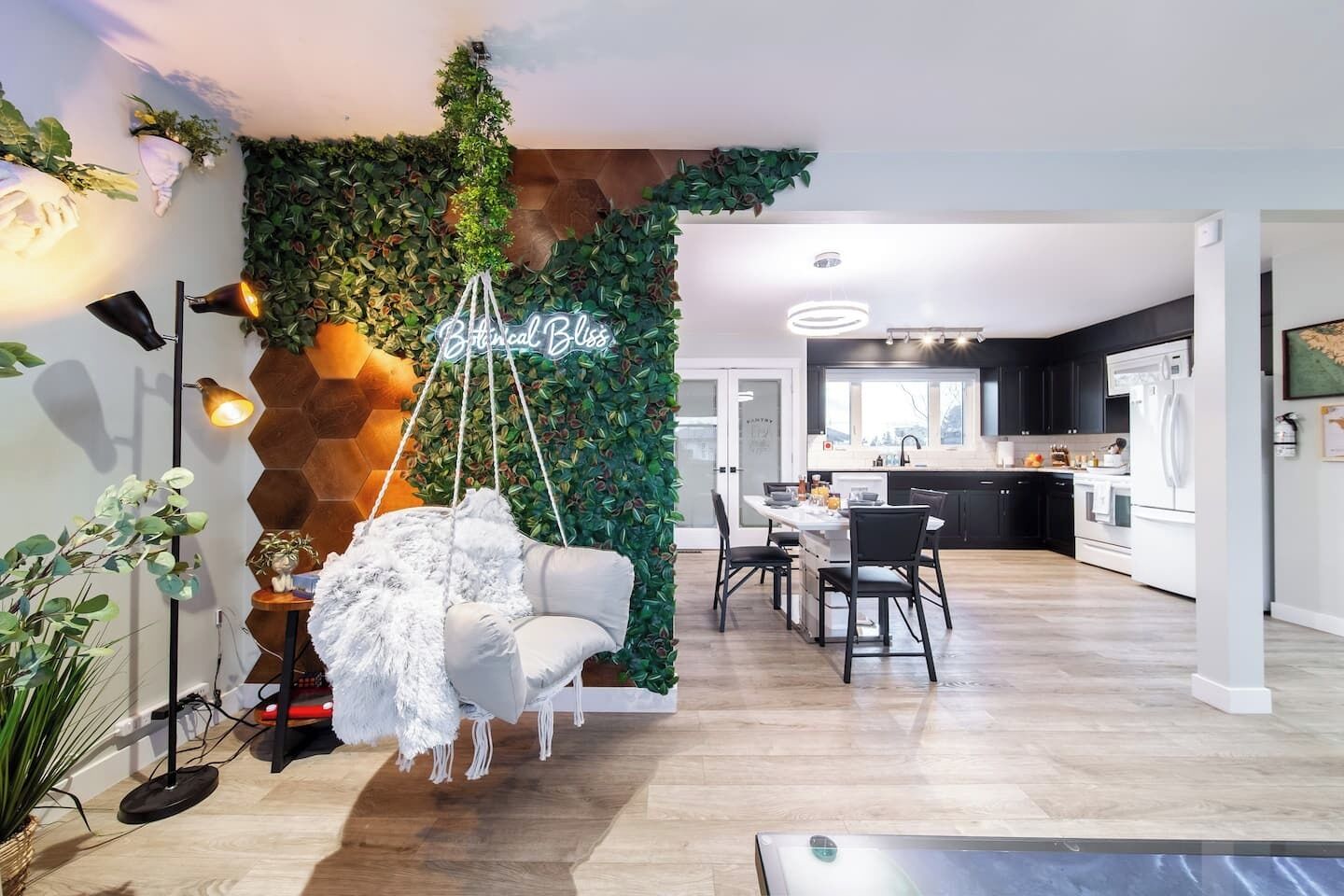 A modern living room with a hanging chair, a neon sign, and a kitchen in the background.