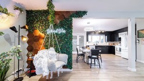 A modern living room with a hanging chair, a neon sign, and a kitchen in the background. - Relax, recharge, and play. Just 15 mins from Downtown Edmonton (Edmonton)
