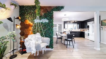A modern living room with a hanging chair, a neon sign, and a kitchen in the background.