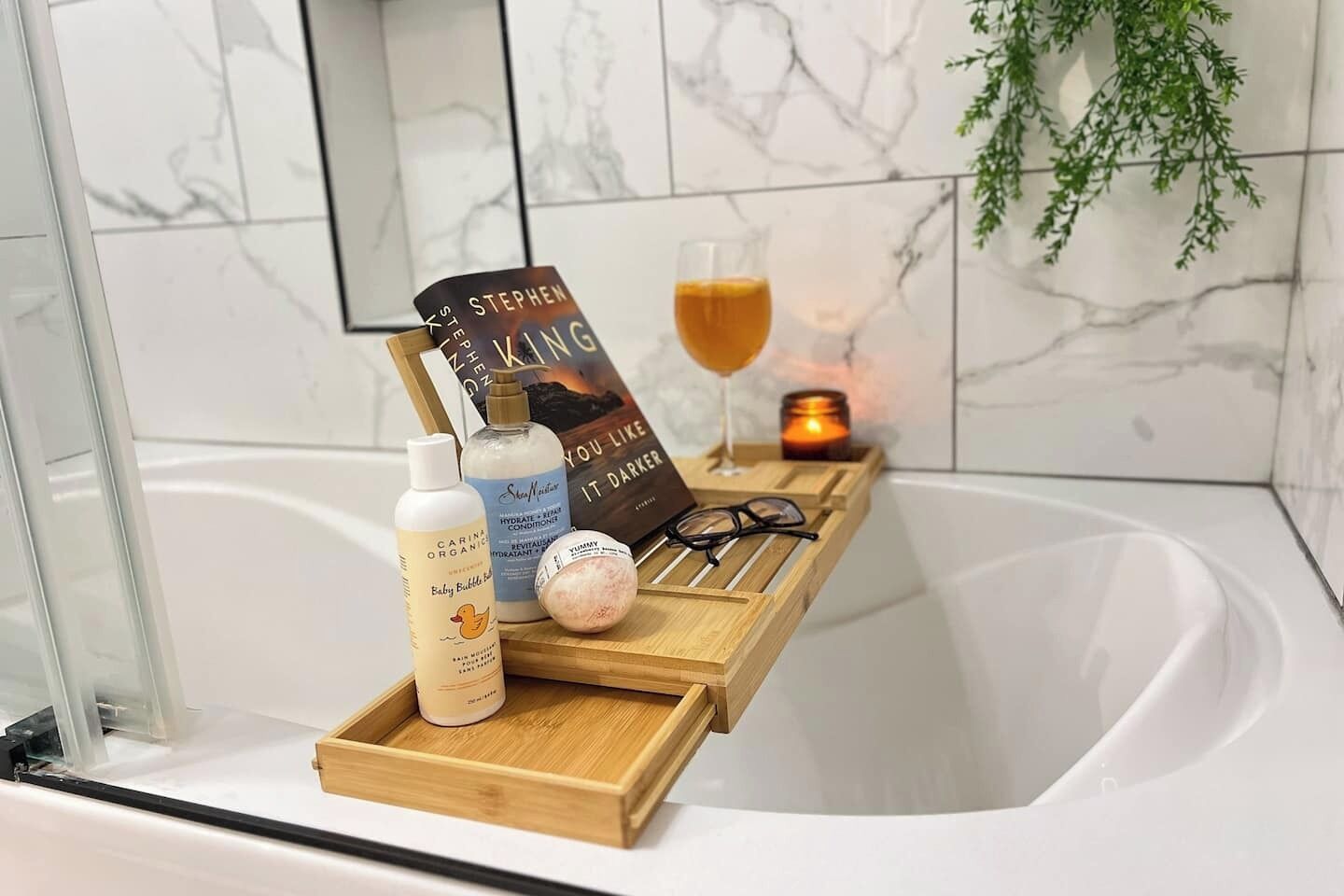 Casa de banho com bandeja de madeira com produtos de higiene, um livro, sumo de laranja e uma vela.