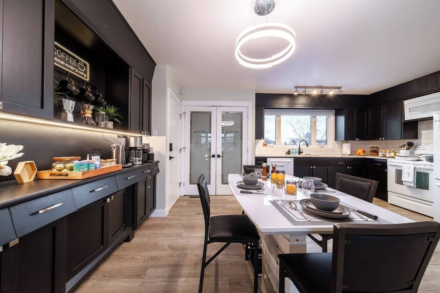 A modern kitchen with dark cabinetry, a central island, and a dining area with a white table set for four.