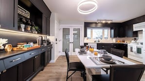 A modern kitchen with dark cabinetry, a central island, and a dining area with a white table set for four. - Relax, recharge, and play. Just 15 mins from Downtown Edmonton (Edmonton)
