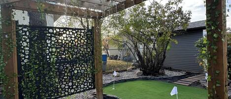 Un jardín con un pérgola, un césped verde y una valla decorativa negra.