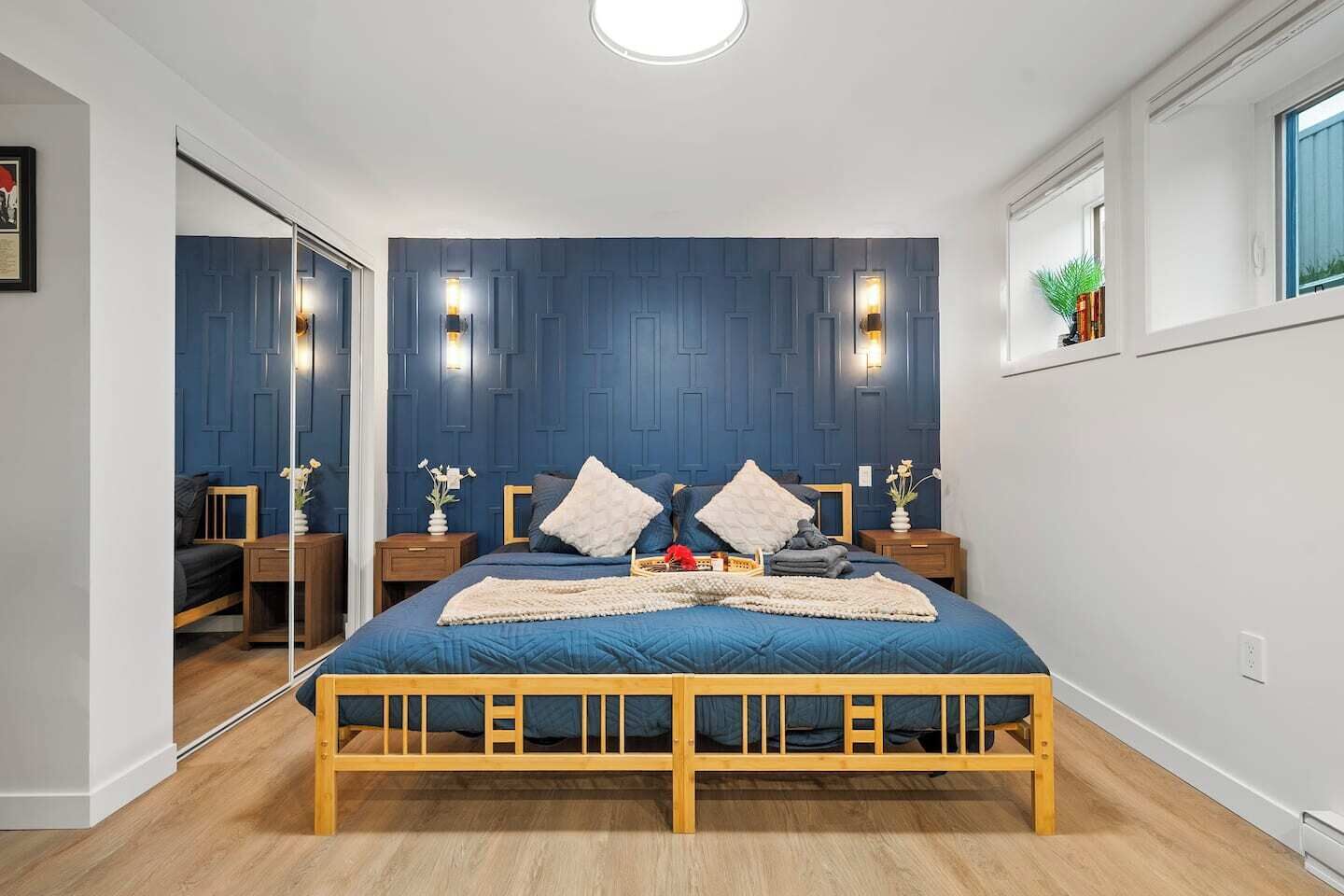 Une chambre à coucher avec un lit en bois, des lambris bleu foncé, deux tables de chevet avec des lampes et une fenêtre donnant sur un paysage agréable.