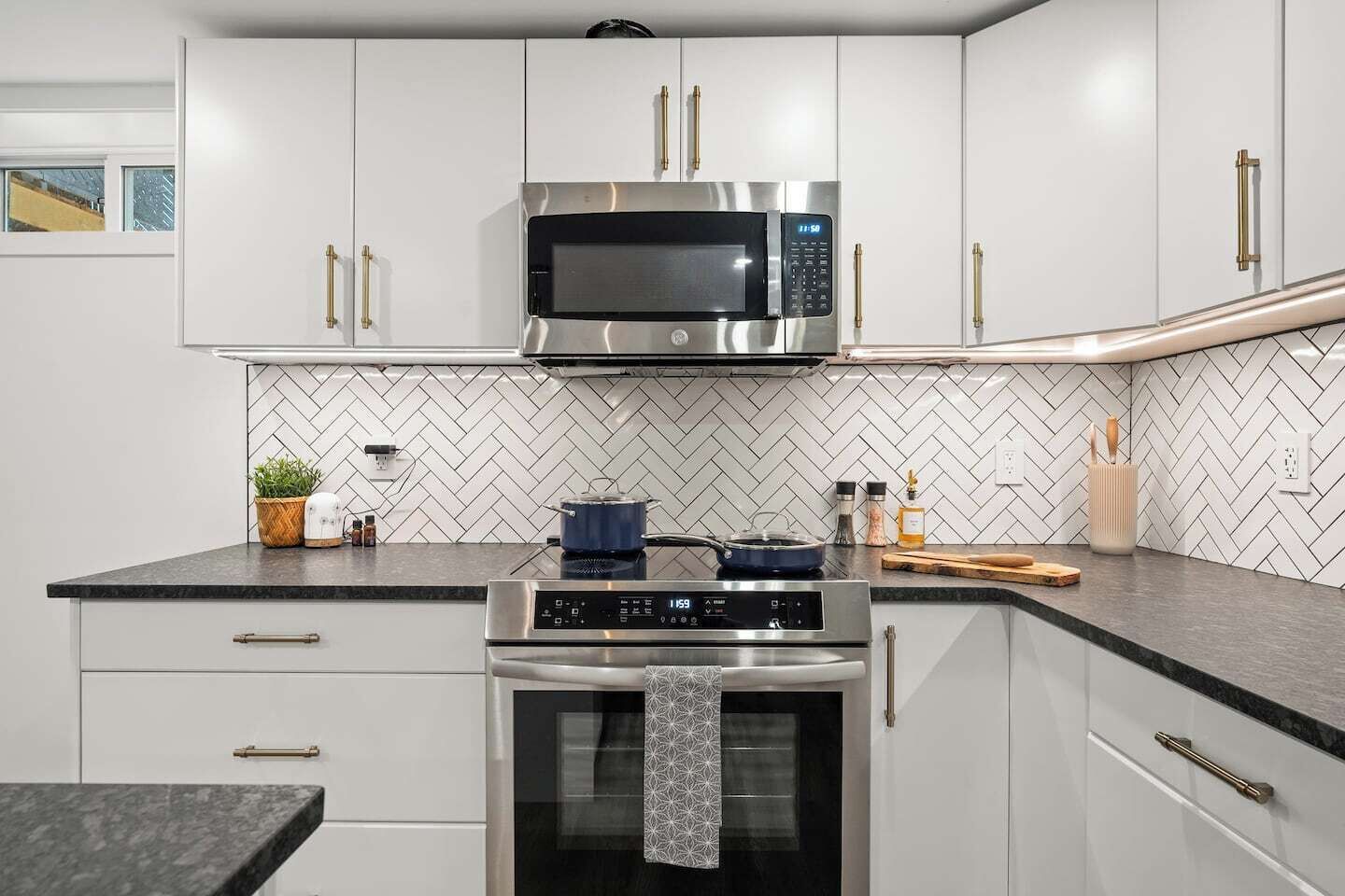 A modern kitchen with white cabinets, a stainless steel microwave, and an oven.