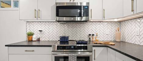 A modern kitchen with white cabinets, a stainless steel microwave, and an oven.