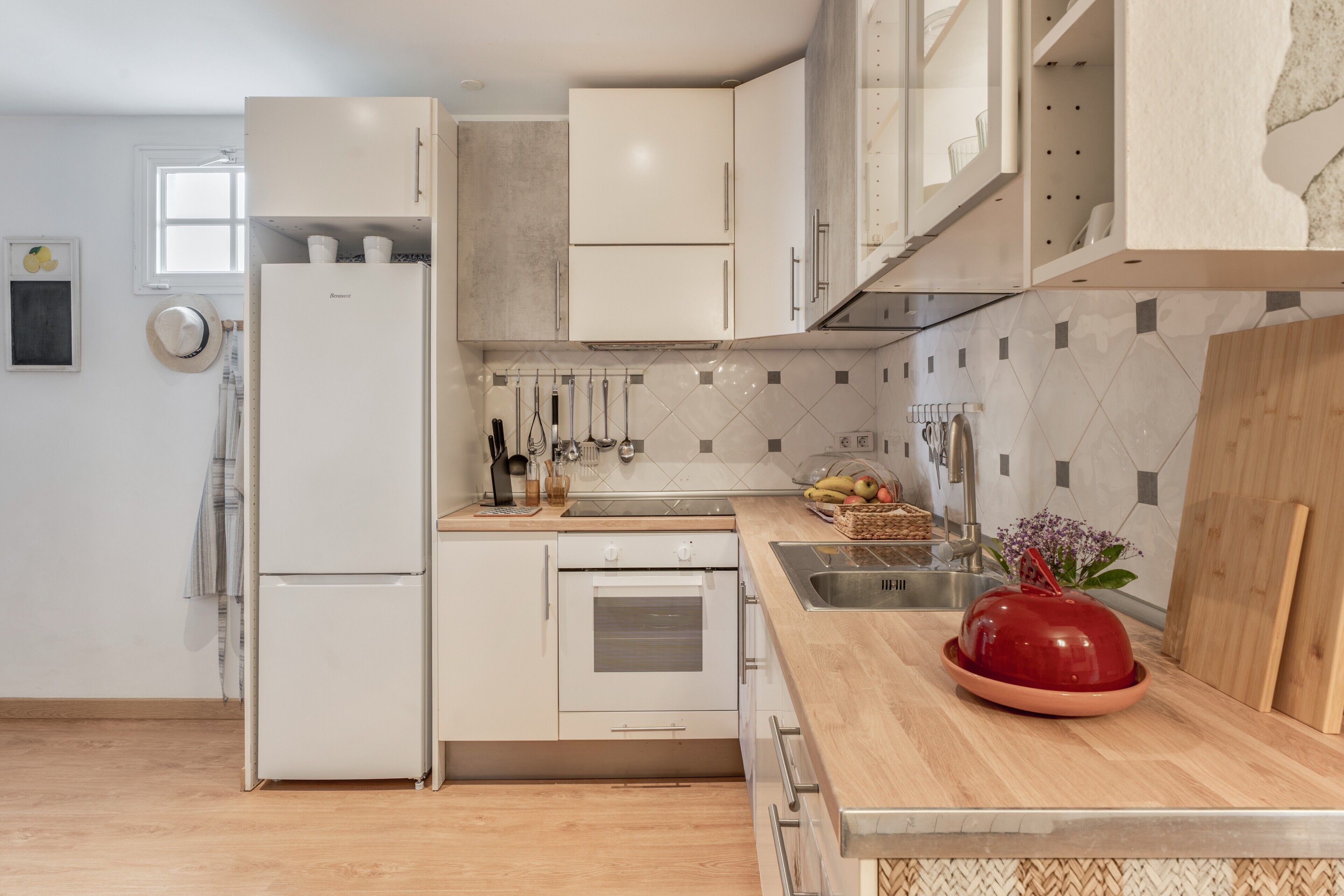 A modern kitchen with white cabinetry, a wooden countertop, a red bowl, and a window with a view.