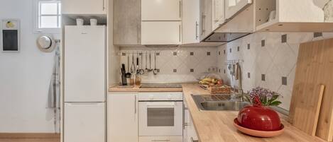 A modern kitchen with white cabinetry, a wooden countertop, a red bowl, and a window with a view.