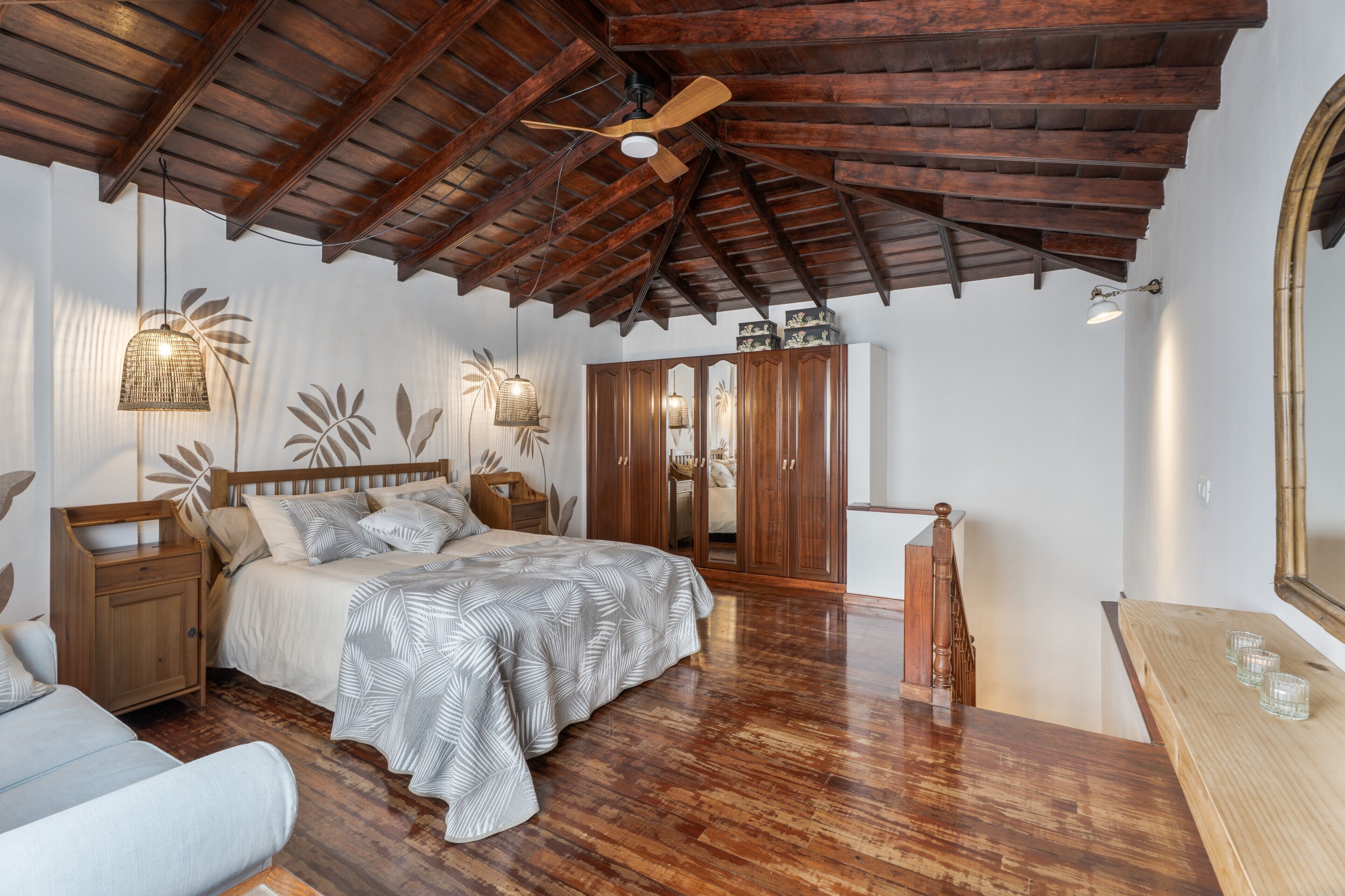 A bedroom with a wooden ceiling, a bed with a patterned bedspread, a nightstand, a dresser, and a mirror.