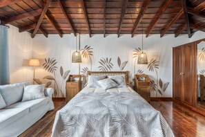 Un dormitorio con una cama, cabecera de madera, dos mesitas de noche, un armario y un sofá.