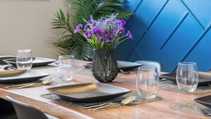 A dining table set with plates, cutlery, and glasses, with a vase of purple flowers in the center. - Pac-Man fun, pet-friendly comfort, and cozy vibes near Downtown Edmonton (Edmonton)