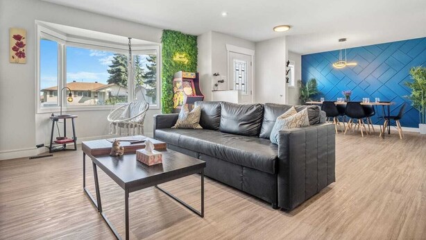 A modern living room with a grey sofa, a coffee table, and a dining area with a blue accent wall. - Pac-Man fun, pet-friendly comfort, and cozy vibes near Downtown Edmonton (Edmonton)