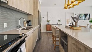 A modern kitchen with wooden cabinets, a stainless steel refrigerator, a built-in oven, and a bar area with stools. - Walk to cafes, Safeway, and trails from this stylish Whyte Ave groundfloor suite (Edmonton)