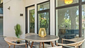 An outdoor seating area with wicker chairs and a round table, large windows, and a potted plant. - Walk to cafes, Safeway, and trails from this stylish Whyte Ave groundfloor suite (Edmonton)