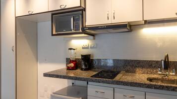 Una cocina moderna con armarios blancos, microondas integrado, licuadora y refrigerador pequeño.